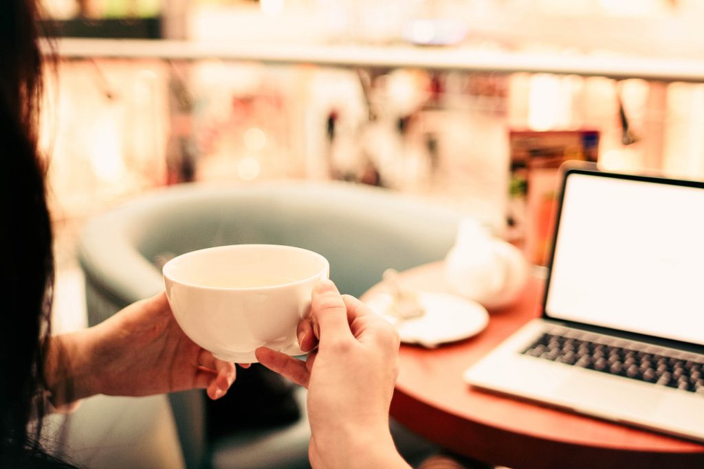 person holding coffee in front of laptop in cafe
